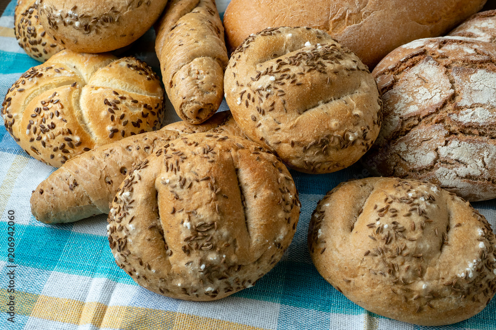 Heap of various bread rolls sprinkled with salt, caraway and sesame. Fresh rustic bread from leavened dough. Assortment of freshly of bakery products