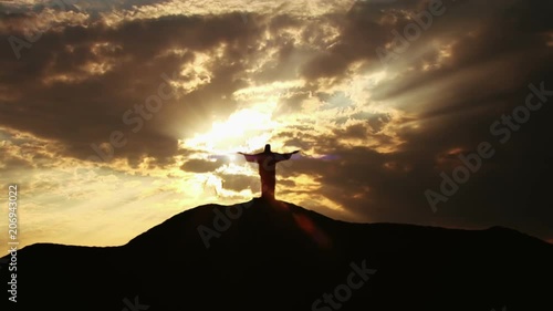 Jesus silhouette standing on hill crest with sun and clouds behind him. photo