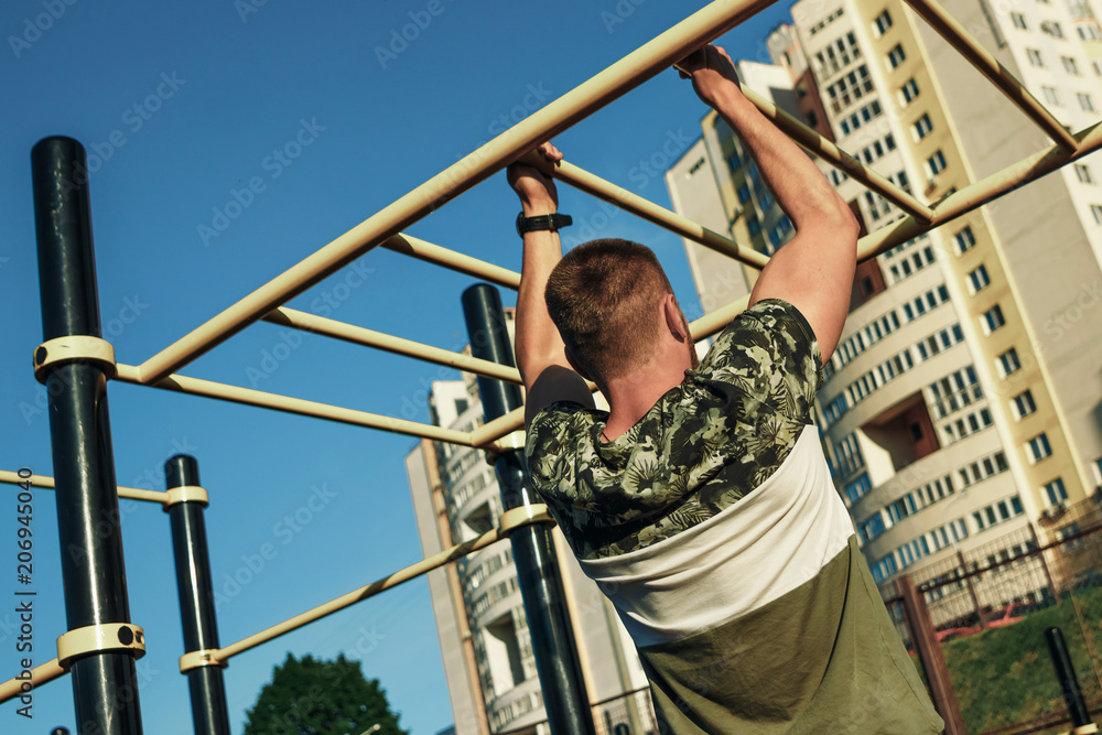 A young man pulls himself up on the sports ground, an athlete, training outdoors in the city. copy space