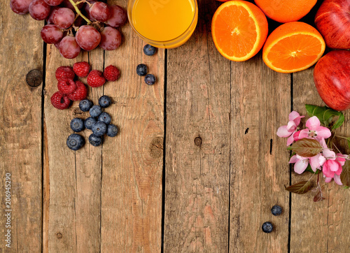 Fototapeta Naklejka Na Ścianę i Meble -  Orange juice, fresh oranges, apples, grapes, raspberries, blueberries and spring flowers on a wooden table - view from above