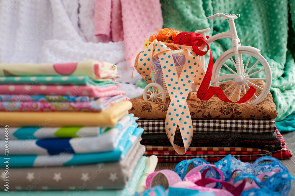 Fototapeta premium A stack of fabric and a sewing tape. Fabric, ribbons, decorative bike on the counter of the store. Fabric for sewing clothes.