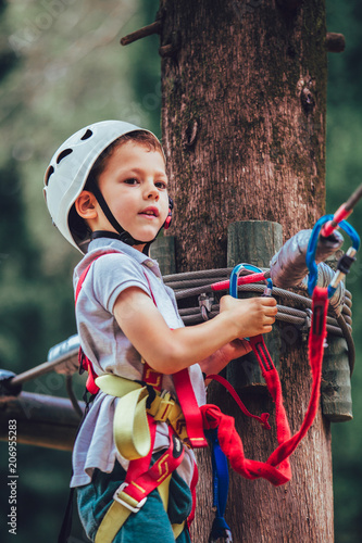 Little boy climbing in adventure activity park with helmet and safety equipment