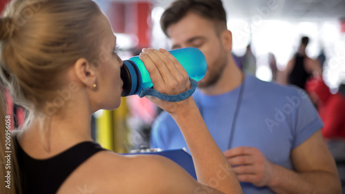 Athlete woman drinking water and listening to coach advice after workout in gym