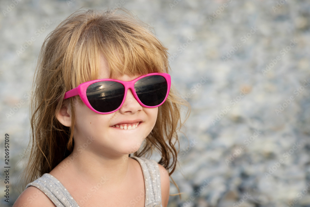 portrait of a charming little blonde girl in pink sunglasses on a pebble beach background portrait of a charming little blonde girl in pink sunglasses on a pebble beach background