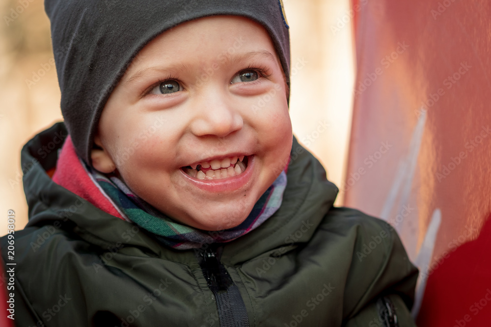 Happy little boy with a cap laughing loudly sitting on a children slide,close up.
Happy little boy with a cap laughing loudly sitting on a children slide,close up.