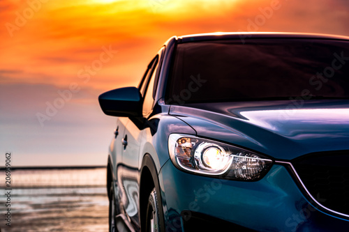 Blue compact SUV car with sport and modern design parked on the beach by the sea at sunset. Environmentally friendly technology. Business success concept. Front view car with open headlamp light. © Artinun