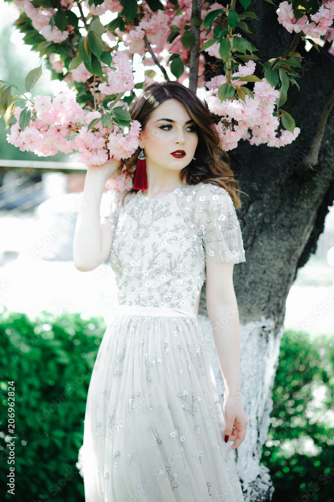 very beautiful girl the bride under a veil, beige wedding dress near the tree Sakura is looking down, nature very beautiful girl the bride under a veil, beige wedding dress near the tree Sakura is looking down, nature