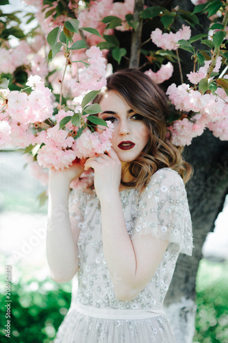 very beautiful girl the bride under a veil, beige wedding dress near the tree Sakura is looking down, nature photo