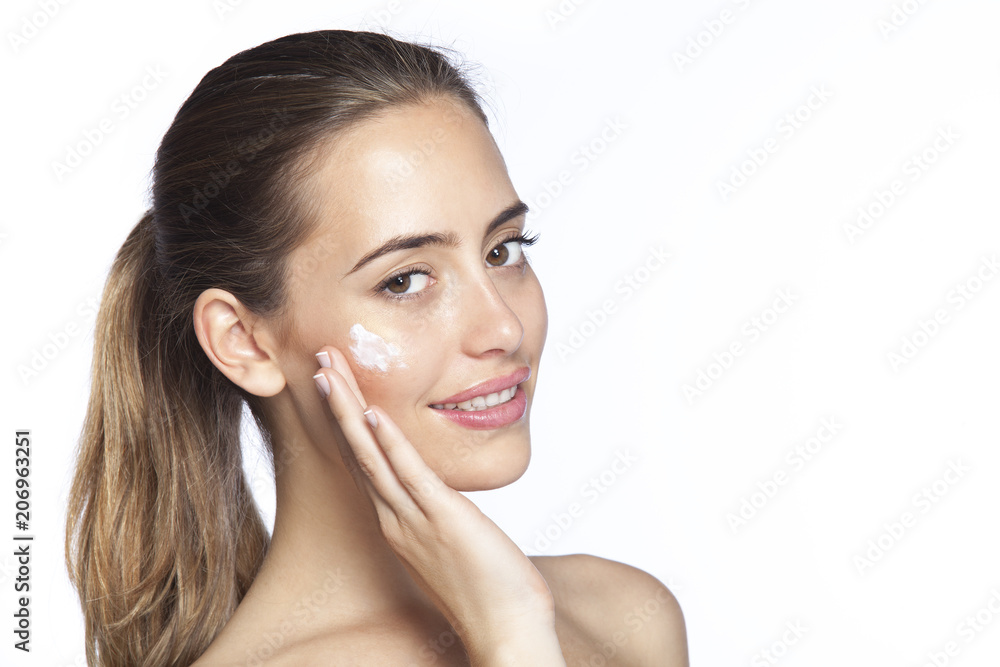 Portrait of smiling beautiful young woman touching skin or applying cream, over white background