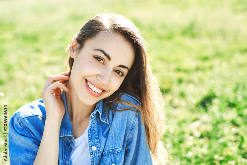 portrait of attractive woman in jeans sitting in a park on the grass at sunny summer day