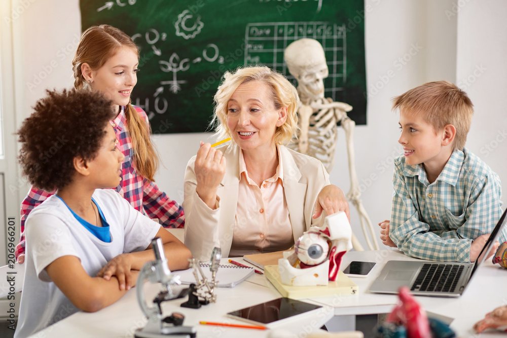 School teacher. Nice delighted woman sitting at the table while having a biology class School teacher. Nice delighted woman sitting at the table while having a biology class