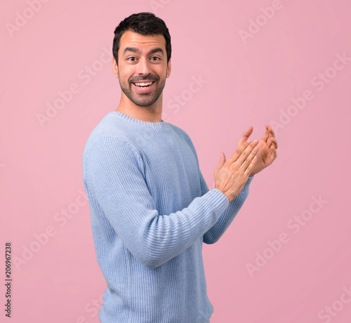 Man with blue sweater applauding after presentation in a conference on pink background