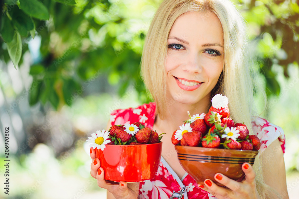 Φωτογραφία young tender blonde woman with strawberries in a bowl, in a green garden a summe