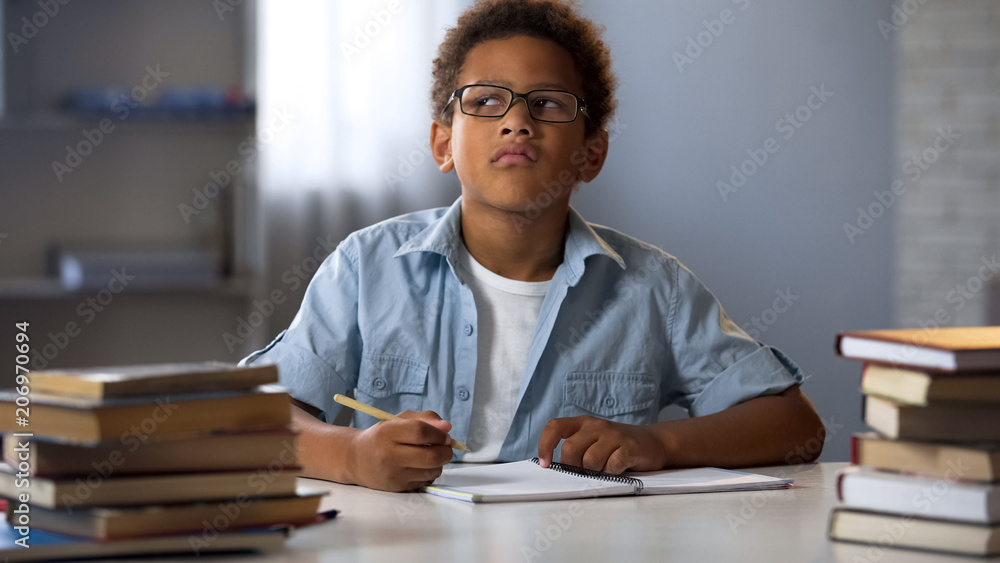Afro-American boy thinking on school essay, smart kid doing homework, education Afro-American boy thinking on school essay, smart kid doing homework, education