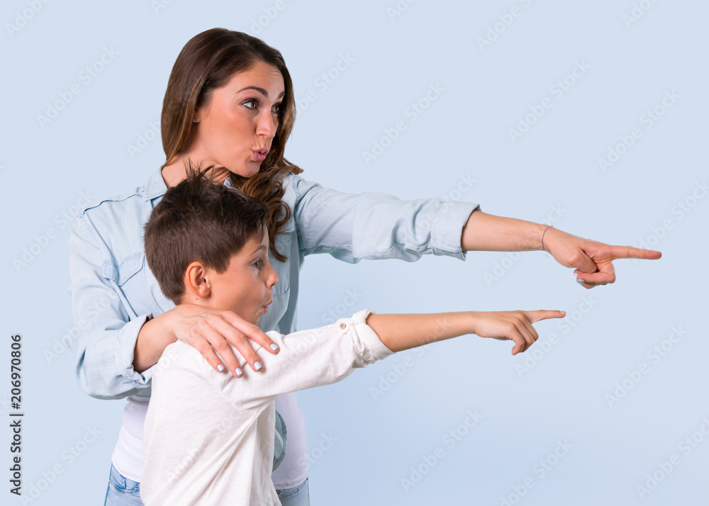 Mother and daughter pointing finger to the side and presenting a product on blue background Mother and daughter pointing finger to the side and presenting a product on blue background