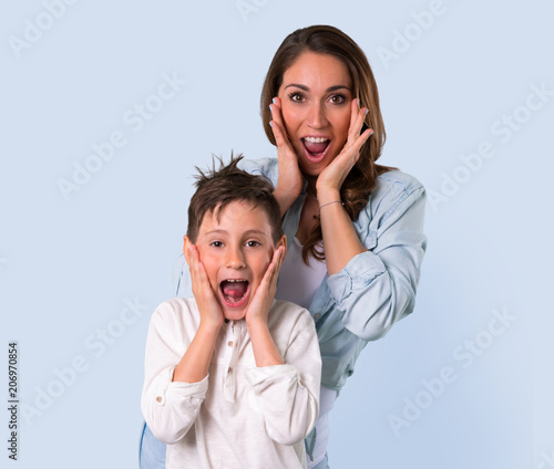 Mother and daughter with surprise and shocked facial expression on blue background