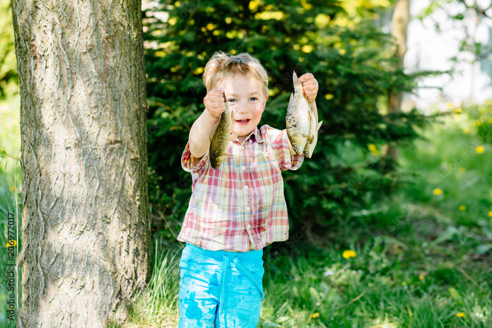 A small child enjoying catch. Little blond boy holding two fishes outside in sunny summer day. Childhood and adventure concept. A small child enjoying catch. Little blond boy holding two fishes outside in sunny summer day. Childhood and adventure concept.