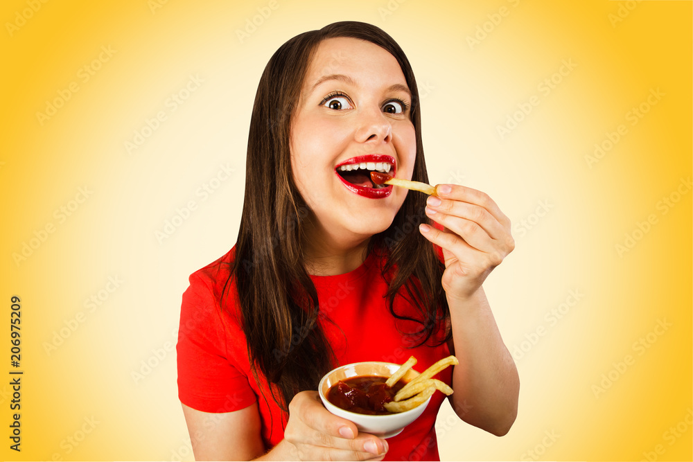 Young girl eating fries with ketchup and smiling. Isolated on yellow background. Young girl eating fries with ketchup and smiling. Isolated on yellow background.