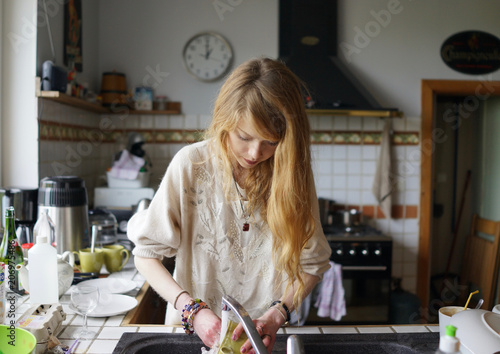 Vászonkép Pretty young woman standing at the kitchen sink, washing-up