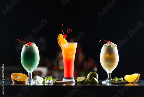 Multi-colored alcoholic cocktails with citrus and berries in glasses of different shapes on the bar.