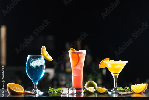 Multi-colored alcoholic cocktails with citrus in glasses of different shapes on the bar.