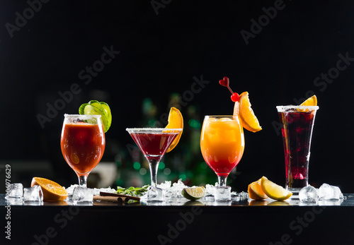 Multi-colored alcoholic cocktails with citrus in glasses of different shapes on the bar.