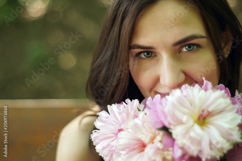 Pretty young beautiful woman on a bench with peony flowers and shining sun. Place for text