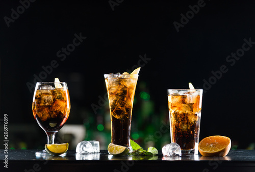 Alcoholic beverages whiskey and cola in glasses of different shapes on the bar table.