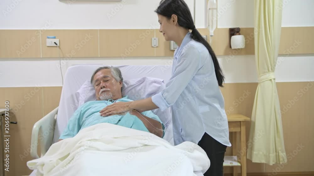 Care taker putting senior patient to bed in hospital. Young beautiful female care taker putting blanket on to her senior male patient to comfort him while he sleeps. Senior care service concept. Care taker putting senior patient to bed in hospital. Young beautiful female care taker putting blanket on to her senior male patient to comfort him while he sleeps. Senior care service concept.