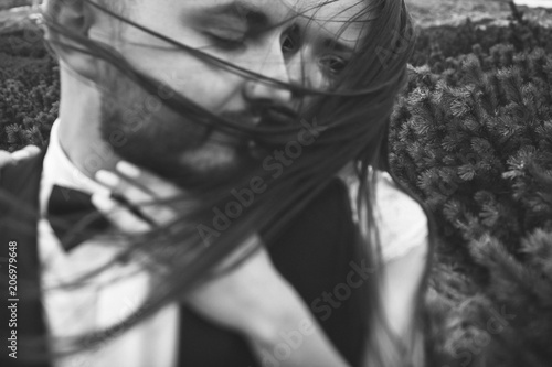 Beautiful close up portrait of sensual wedding couple hugging outdoors in the needleleaf forest in mountains. Hair in the wind. Black and white shot