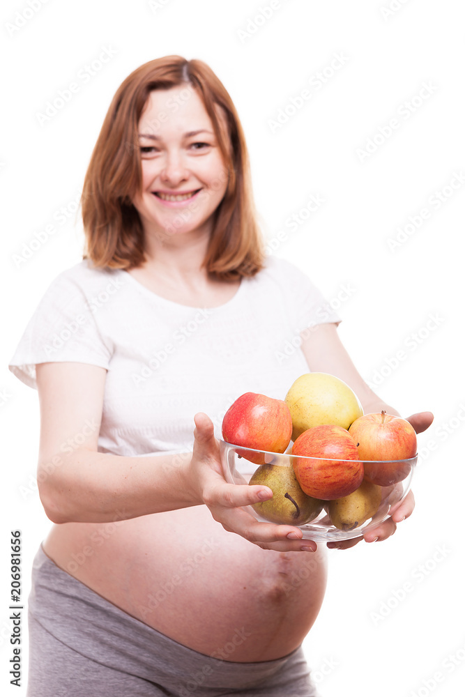 Pregnant woman smiling to the camera and holding a glass bowl with fruits in her hands isolated over white background Pregnant woman smiling to the camera and holding a glass bowl with fruits in her hands isolated over white background