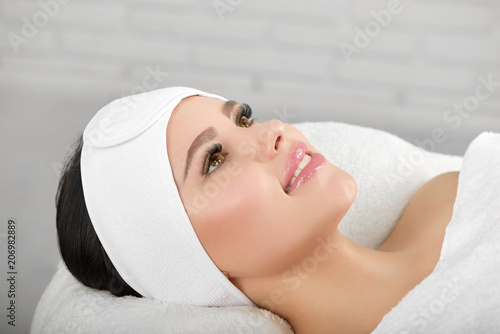 Smiling woman lying on white cosmetological coach wearing headbandage. Waiting for beaty salon procedures and professinal master. Smoth, young, healthy skin. Beatiful face. photo