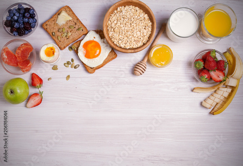 Breakfast served with coffee, orange juice, oat cereal, milk, fruits, eggs and toast. Balanced diet. Morning sweet and savory meal, food background. overhead, horizontal