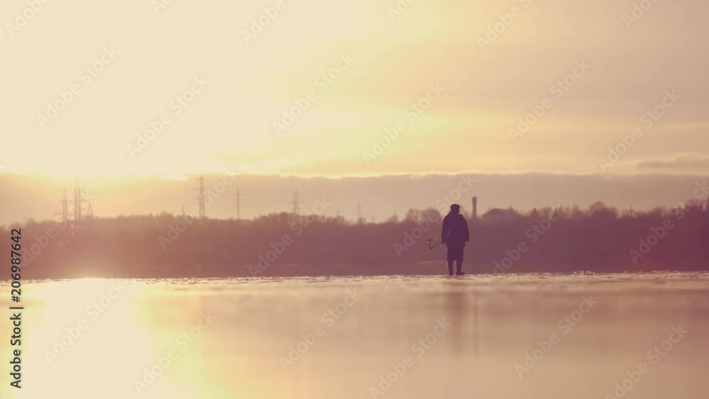 Fisherman walking on lake ice with an ice drill and winter fishing gear. Slow motion video