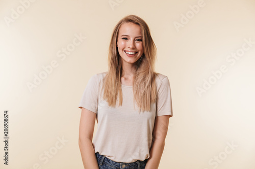 Image of beautiful pleased woman 20s wearing casual t-shirt laughing and looking at you with happy smile, isolated over beige background in studio