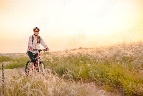 Young Woman Riding Mountain Bikes in the Beautiful Field of Feather Grass at Sunset. Adventure and Travel.