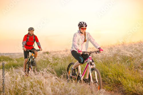 Young Couple Riding Mountain Bikes in the Beautiful Field of Feather Grass at Sunset. Adventure and Family Travel.