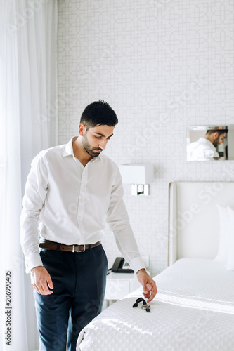 Thoughtful Indian man stands in a white hotel room in the morning