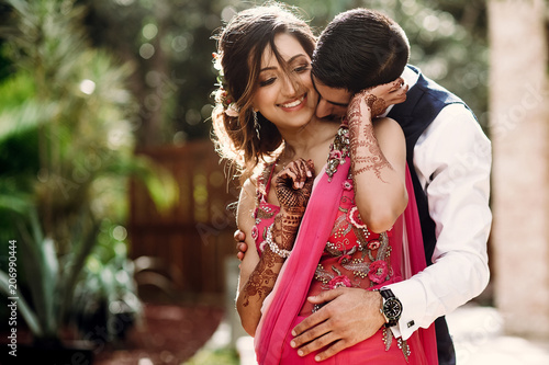 Hindu groom kisses bride in a sari tender standing in the morning park photo