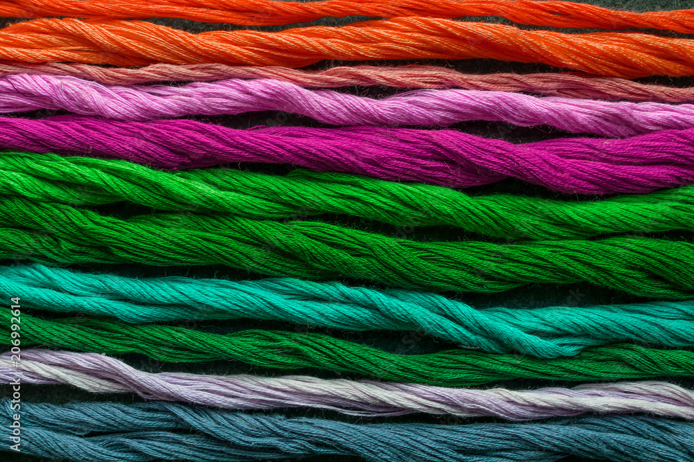 Bright multicolored embroidery thread yarns. Skeins of multicolored orange, pink, purple, green, turquoise, blue embroidery threads on dark felt canvas. Handmade embroidery sewing background