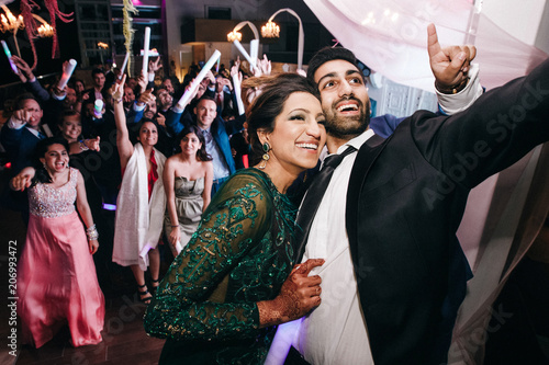 Indian wedding couple takes selfie on the phone standing with their guests in the restaurant