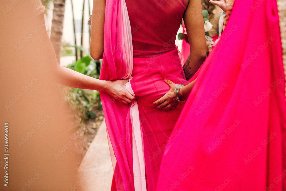Bridesmaids grab Indian bride's hips walking around the garden
