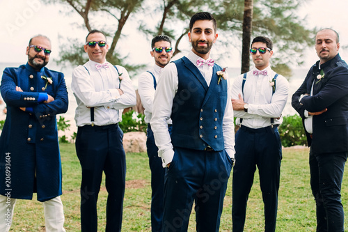 Handsome Indian groom and groomsmen in classy suits pose together on the lawn photo