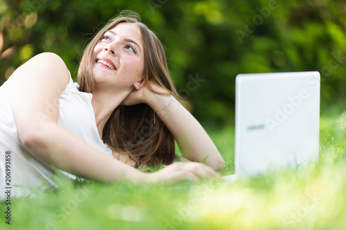 Young dark blonde girl studying in a park with a laptop