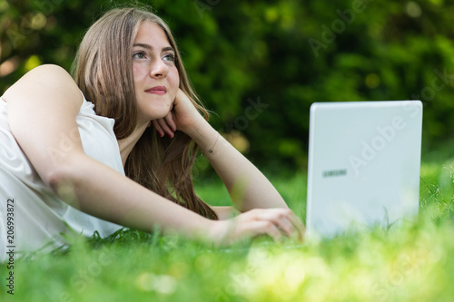 Young dark blonde girl studying in a park with a laptop