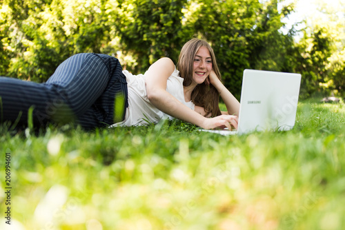 Young dark blonde girl studying in a park with a laptop
