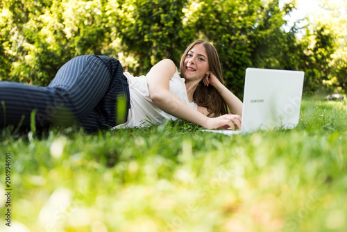 Young dark blonde girl studying in a park with a laptop