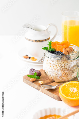 Healthy breakfast in glass mason jar with oat flakes, granola, milk, dry fruits and nuts, dates, honey, orange juice, eggs for morning fitness on wooden board platter on white background isolated