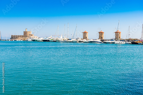 Windmills, boats and St. Nicoaus fortress in Mandraki harbor in City of Rhodes (Rhodes, Greece)