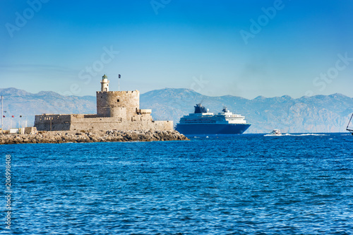 Cruise ship behind lighthouse in Mandraki harbor in City of Rhodes (Rhodes, Greece)